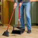 A person sweeping the floor with a Libman deluxe lobby broom and dust pan.
