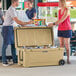 A man and woman standing next to a CaterGator outdoor cooler full of bottles.