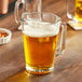 An Acopa glass beer pitcher on a table in a bar full of beer.