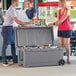 A man and woman standing next to a CaterGator outdoor cooler filled with bottles.