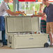 Two men standing next to a tan CaterGator outdoor cooler filled with bottles.