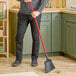 A person using a Libman commercial angle broom to sweep a professional kitchen floor.