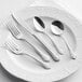 A plate with Acopa stainless steel flatware including a spoon, fork, and knife.
