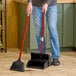 A person using a Libman Lobby Broom and Dustpan to sweep a floor.