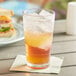 A Choice plastic highball glass filled with liquid and ice on a table with a sandwich.