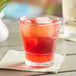 A Choice plastic stackable rocks glass filled with red liquid and ice on a table.