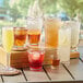 Choice plastic rocks glasses filled with brown, orange, and clear drinks on a table.