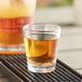 A Choice plastic shot glass filled with brown liquid on a metal tray.