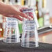 A hand holding a stack of clear plastic Choice double rocks glasses.