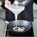 A person using a Choice white plastic funnel to pour liquid into a pan.