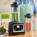 A person in an apron using an AvaMix commercial blender to make a green smoothie.