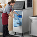 A woman in an apron using a Hoshizaki ice storage bin to fill a blue container with ice.