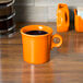 A Tangerine Fiesta china mug filled with coffee on a table.