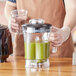 A person holding a Waring blender with green liquid in it.