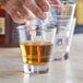 A hand pouring whiskey into an Acopa Select flared rocks glass on a table.