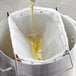 A person using a 6" deep fryer oil filter bag to pour liquid into a metal container.