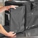 A person opening a black Vesture thermal chafer pan carrier bag to reveal a white container inside.