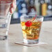 A person holding an Acopa Select flared rocks glass filled with ice and alcohol with a cherry on top.