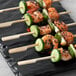 Bamboo skewers with shrimp and cucumber on a table.