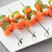 A close-up of a skewer with salmon and cucumber on a white plate.