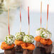 A plate of meat appetizers with red bamboo skewers on a table.