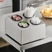 A stainless steel flatware organizer with black perforated plastic cylinders holding straws and condiments on a counter.