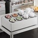 A stainless steel flatware organizer with black perforated plastic cylinders holding utensils on a counter.