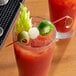 A glass of red liquid with a Bamboo Loop Food Skewer holding a green olive and red garnish.
