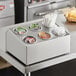 A Choice stainless steel flatware organizer with gray perforated plastic cylinders on a counter with condiments and sugar containers.