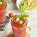 Two glasses of red drinks with a cherry tomato and jalapeno on a bamboo skewer.