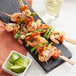 A Bamboo by EcoChoice skewer with grilled shrimp and vegetables on a black plate.