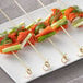 Bamboo food picks skewered with smoked salmon, dill, and cucumber on a plate.