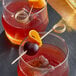 Two glasses of red liquid with orange slices and a cherry on a Bamboo Loop Food Pick on a table in a cocktail bar.