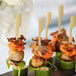 A black plate with a group of food skewered on green bamboo paddles.