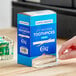 A person's hand pulling a plastic toothpick out of a blue and white Choice dispenser box.