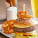 A burger with "Medium Well" labeled on a bamboo pick alongside onion rings and a beer.