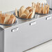 A stainless steel flatware organizer with blue perforated plastic cylinders holding wooden spoons and forks.