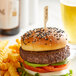 A burger with a Bamboo by EcoChoice "Rare" Meat Marker on top, served with fries on a plate.