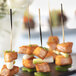 A hand holding a piece of celery with a black bamboo skewer on a plate of food.