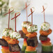 A table with a white and green plate of food on red bamboo skewers.