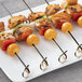 A plate with several black bamboo skewers of food on it.