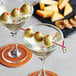 A pair of martini glasses with red bamboo knot skewers holding green olives.