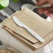 A person cutting a piece of bread with a Preserve compostable knife on a table.