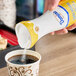 A hand pouring Domino Quick-Dissolve Superfine Sugar into a cup of coffee.