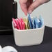 A hand putting a sugar packet into a white Tuxton sugar caddy on a hotel buffet counter.