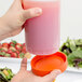 A person pouring pink liquid into a Carlisle Store 'N Pour container with an orange cap.