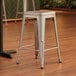 A Lancaster Table & Seating silver metal backless counter height stool on a wood floor.