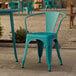 A teal Lancaster Table & Seating outdoor arm chair on a stone patio.