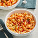 A bowl of Barilla medium shell pasta with shrimp and tomato sauce on a white background with a fork.