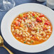 A bowl of pasta soup with vegetables on a white background.